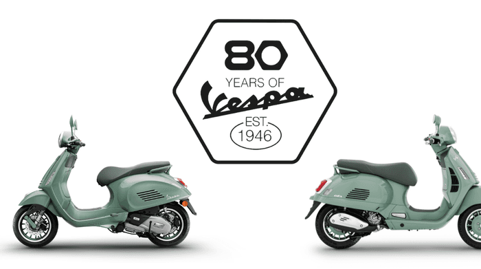 A pair of mint green Vespa scooters positioned side by side, with an emblem celebrating "80 Years of Vespa" established in 1946 displayed between them.
