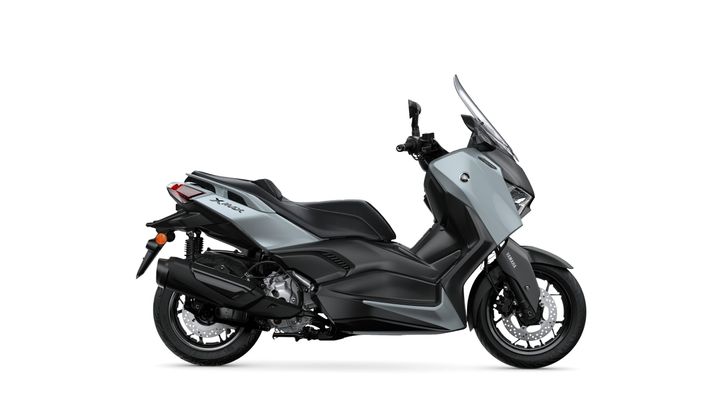 A sleek gray Yamaha XMAX scooter viewed from the side, showcasing its modern design, black seat, and prominent features like a windshield and sporty wheels.