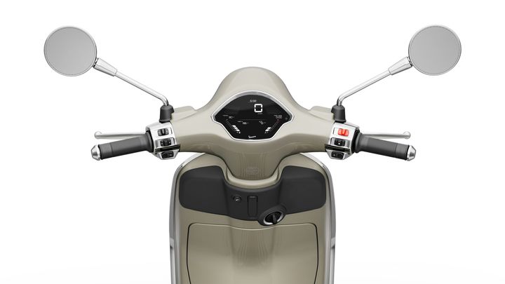 Close-up view of the handlebars of a scooter, featuring round mirrors, a digital display in the center, and control levers on both sides. The scooter has a light beige color with a sleek design.