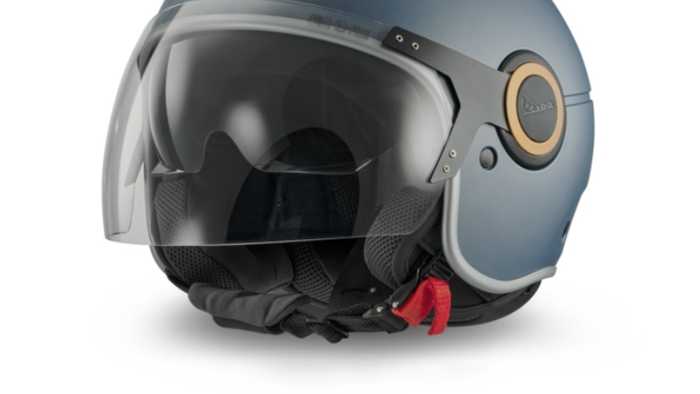 A matte blue motorcycle helmet with a clear visor, side ventilation, and a brown emblem, featuring a red chin strap.