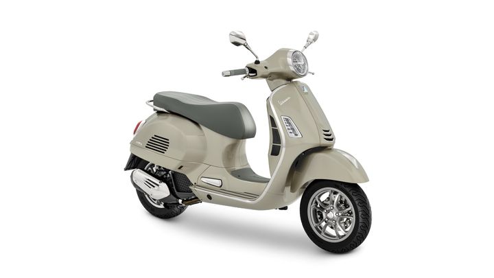 A beige Vespa scooter with a grey seat, showcasing a sleek design and chrome accents, parked on a white background.