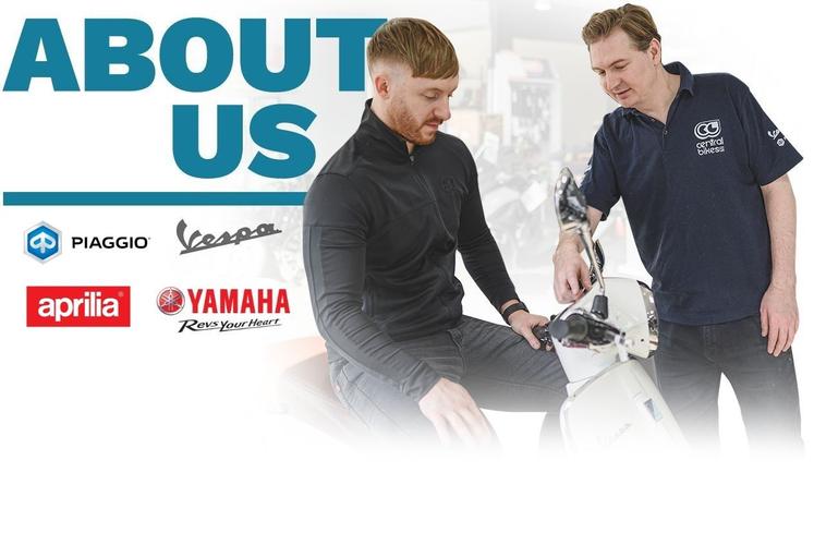A man in a black jacket sits on a scooter while another man in a navy polo shirt points to the scooter's features, with logos of Piaggio, Vespa, Aprilia, and Yamaha displayed prominently above them. The text "ABOUT US" is featured in large, bold letters at the top.