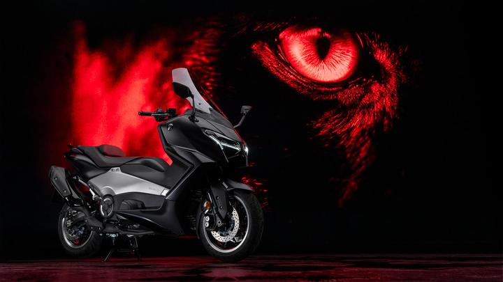 A sleek black motorcycle is prominently positioned against a dramatic backdrop featuring an intense red eye and smoky effects. The bike showcases modern design elements and is partially illuminated by soft lighting.