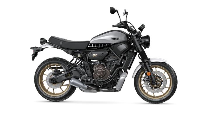 A Yamaha XSR700 motorcycle in a sleek black and silver color scheme, featuring an exposed frame and gold-accented wheels, stands on a white background.