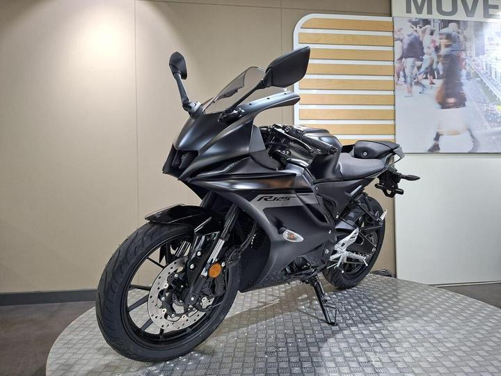 A sleek black motorcycle displayed on a circular platform, with modern features and a minimalist background.