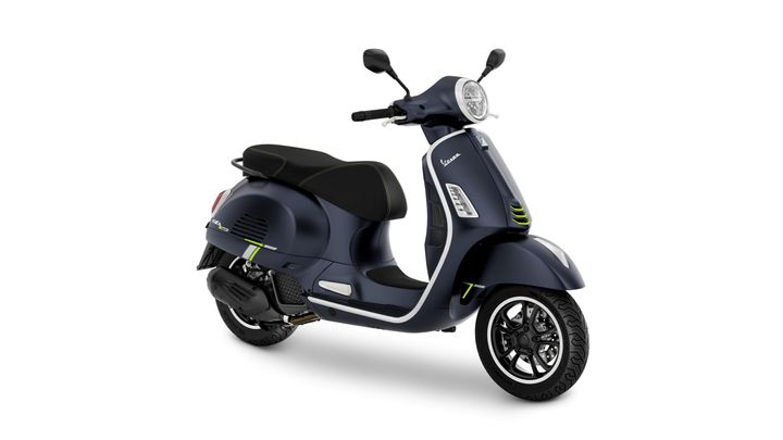 A blue Vespa scooter with black seat and green accents, positioned at a slight angle to showcase its design and features.