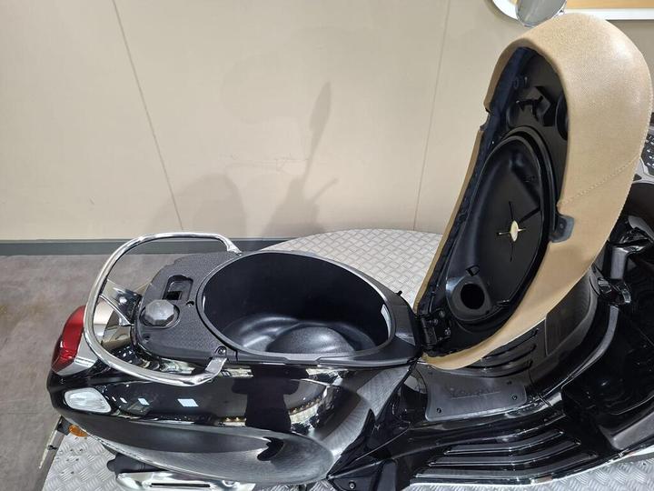 A close-up view of the storage compartment of a black scooter, with the seat lifted to reveal the inner space.
