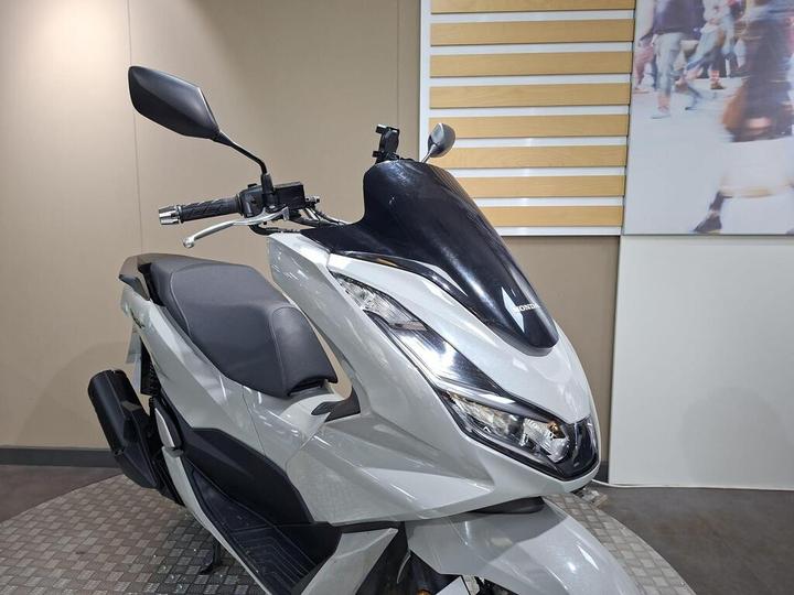 A close-up view of a gray Honda scooter with a sleek design, featuring a black windshield, a modern headlight, and a minimalist seat, displayed on a circular platform against a neutral background.