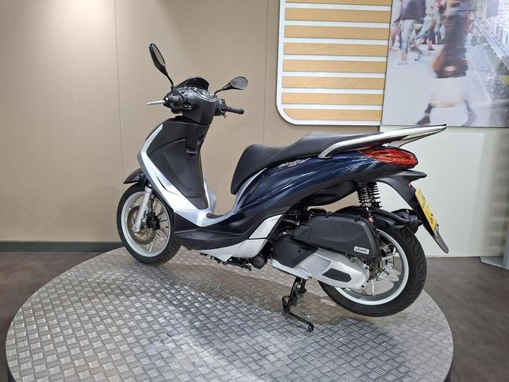 A sleek scooter with a black and white design, positioned on a circular gray platform, against a neutral wall backdrop.