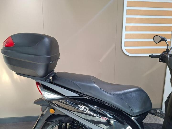 A black scooter with a sleek design, featuring a mounted rear storage box and a comfortable seat, set against a neutral backdrop.