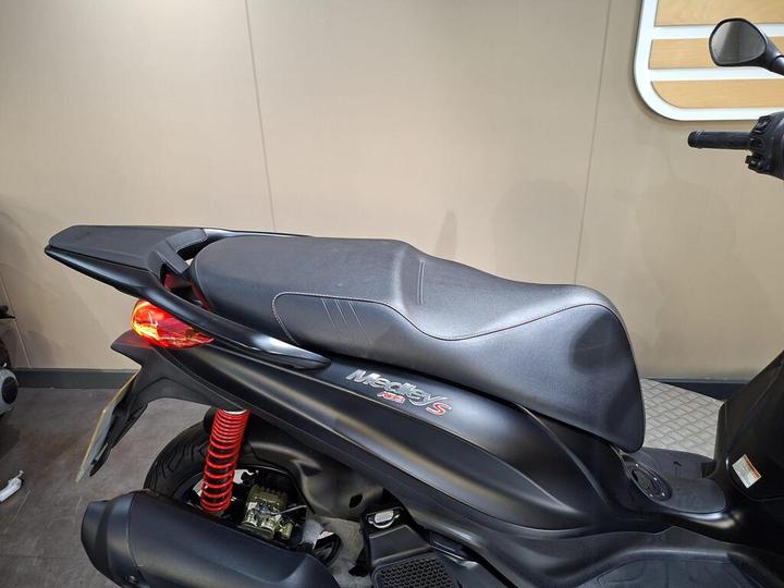 A close-up view of the black seat of a motorcycle, featuring stylish stitching and a sleek design, with a red shock absorber visible beneath.