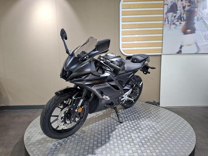 A sleek black sports motorcycle displayed on a circular platform in a modern showroom setting.