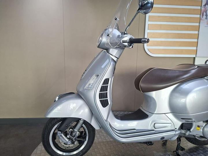 A silver scooter with a brown seat parked against a minimalist background.