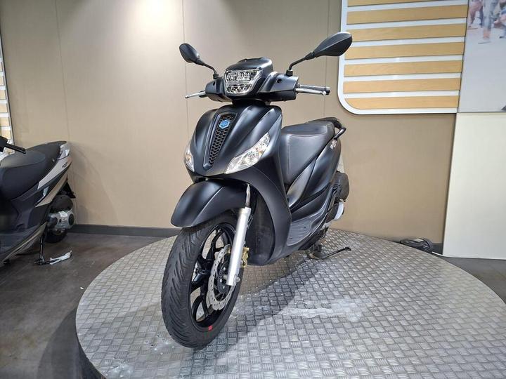 A sleek black scooter showcased on a circular platform, highlighting its modern design and features, set against a neutral wall background.