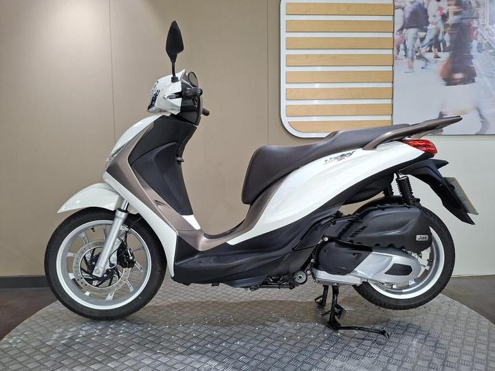 A sleek white scooter with a brown seat displayed on a textured gray surface against a neutral background.