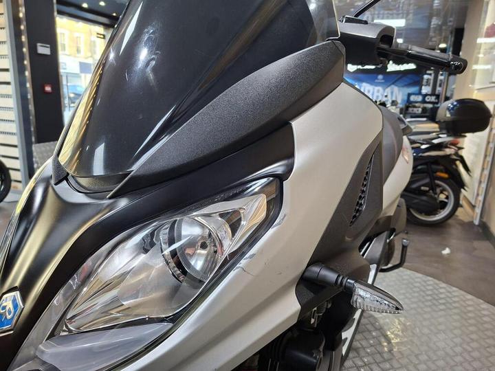 Close-up view of a sleek motorcycle featuring a prominent headlight and a windscreen, showcased in a well-lit retail environment.