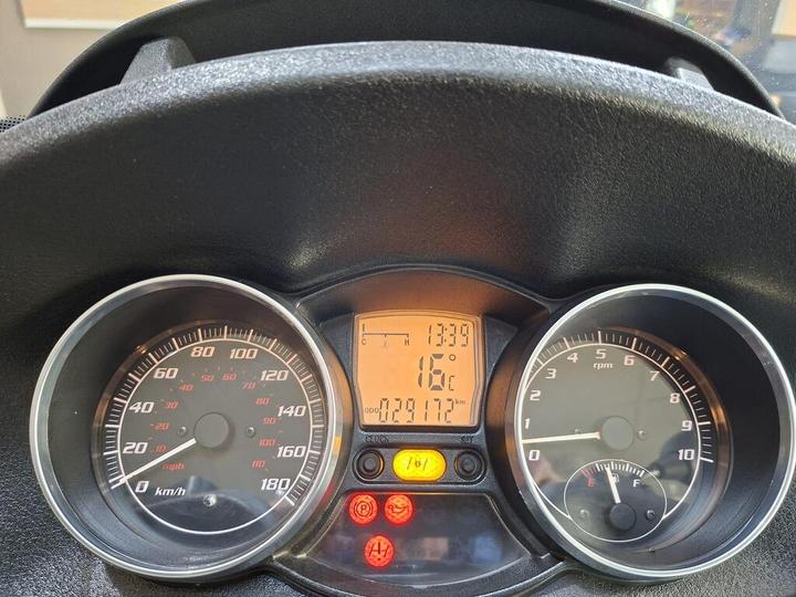 A close-up view of a vehicle's dashboard displaying speedometer, tachometer, and digital readout, showing a speed of 0 km/h, RPM, temperature at 16°C, and an odometer reading of 7917 km, along with warning lights illuminated.