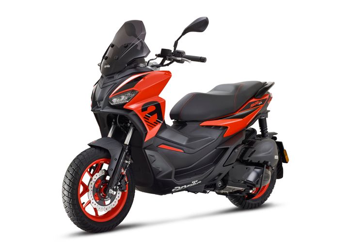 A vibrant orange and black scooter with a sporty design, featuring a windshield, bold graphics, and red accents on the wheels. The scooter is positioned at an angle, showcasing its side profile, seat, and front wheel.