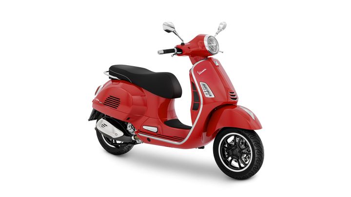 A stylish red Vespa scooter with a black seat, displayed at an angle showing its front and side features, set against a white background.