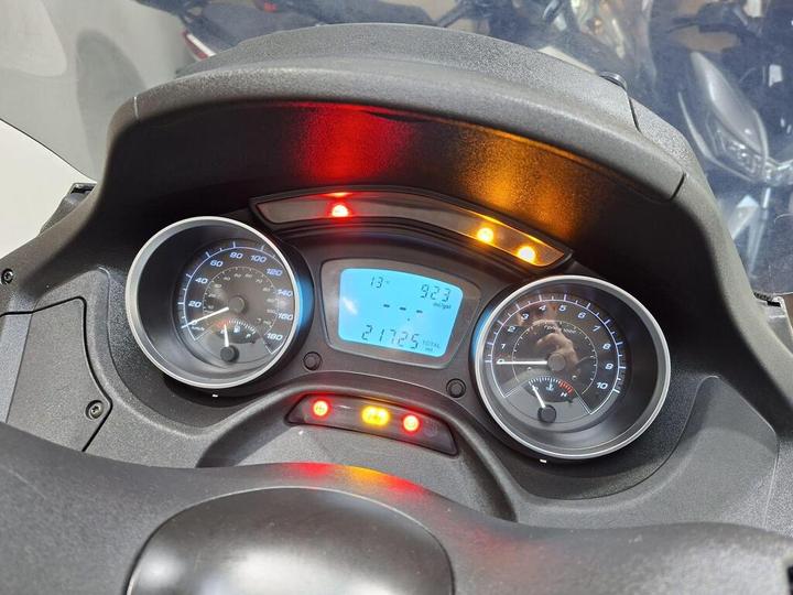 Close-up of a motorcycle dashboard displaying various gauges: a speedometer on the left, an odometer, and a fuel gauge on the right, with warning lights illuminated. The current speed reads 13 mph and the total mileage shows 21725 miles.