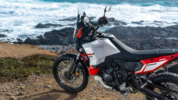 A Yamaha motorcycle parked on a rocky coastline with crashing waves in the background, showcasing its sleek design and off-road tires.