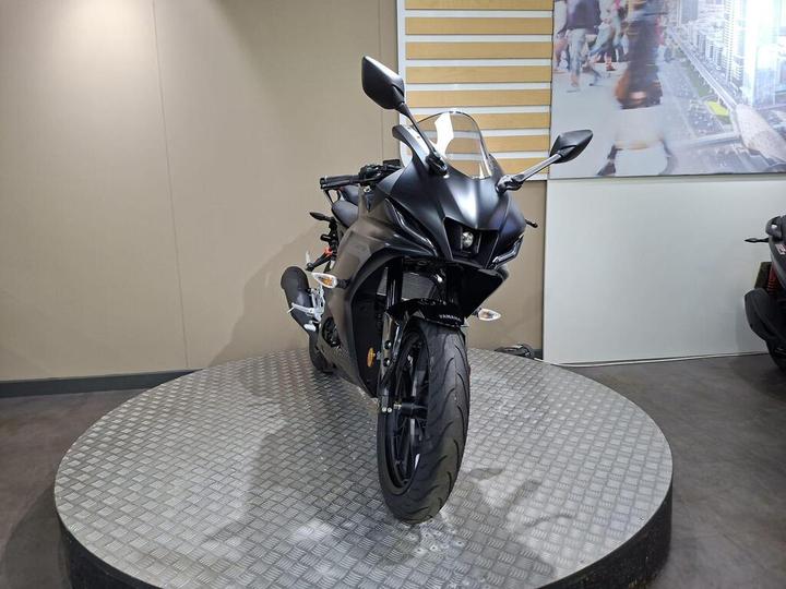 A sleek black motorcycle displayed on a circular platform in a modern showroom, featuring aerodynamic design and aggressive styling.