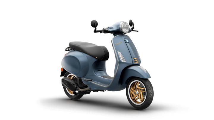 A blue vintage-style scooter with a sleek design, featuring a black seat and gold-accented wheels, positioned at an angle against a white background.