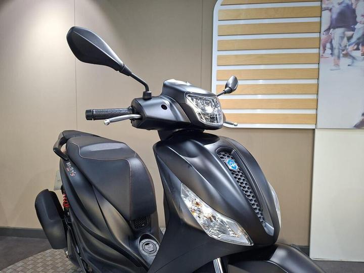 Close-up view of a matte black scooter, highlighting the handlebars, mirrors, and front headlight, against a neutral background with subtle textures.