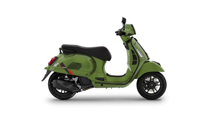 A green Vespa scooter positioned side-on with a modern design, featuring a black seat and stylish wheel spokes, set against a white background.