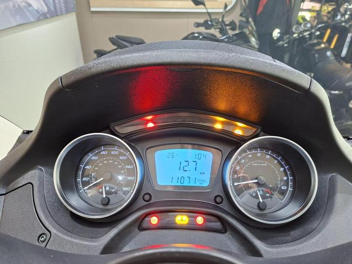 Dashboard of a scooter displaying speedometer, odometer, and warning lights. The speedometer shows a speed of 26 km/h, the odometer reads 1,107 miles, and the digital display shows a voltage of 12.1.