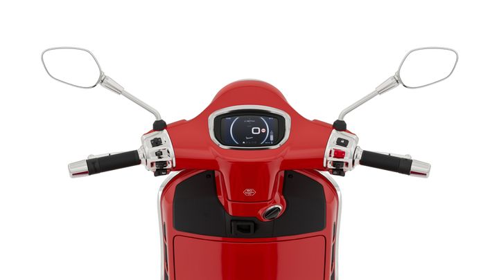A close-up view of the handlebars of a red scooter, featuring digital display, control buttons, and mirrors on either side.
