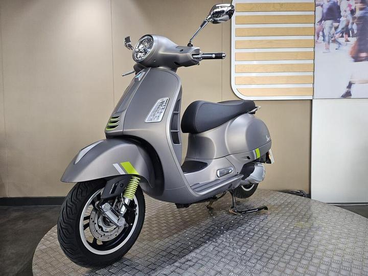A sleek gray scooter with green accents displayed on a textured platform against a neutral background.