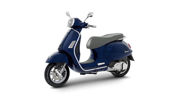 A blue scooter with a sleek design and gray seat, viewed at an angle that showcases its front and side profile.