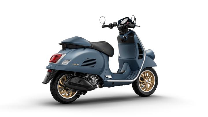 A blue scooter with gold rims and a black seat, showcasing its retro design and sleek profile, positioned on a white background.