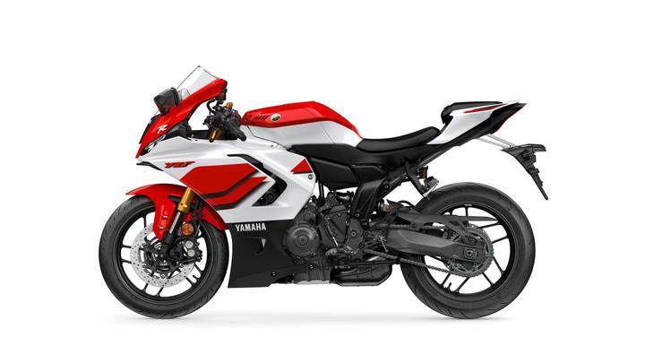 A side view of a red and white Yamaha motorcycle, featuring sleek lines, a sporty design, and a prominent front fairing. The model showcases a modern aesthetic with black accents, a racing-style seat, and high-performance tires.