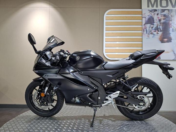 A sleek black Yamaha R125 motorcycle displayed in a showroom, featuring a modern design with a sporty stance and detailed components.