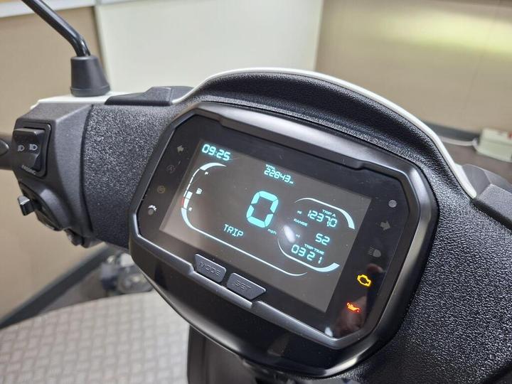 A close-up view of a scooter's digital dashboard displaying speed (0 mph), trip time (12:30), distance (22943 miles), and fuel range (52 miles), with various indicator lights.