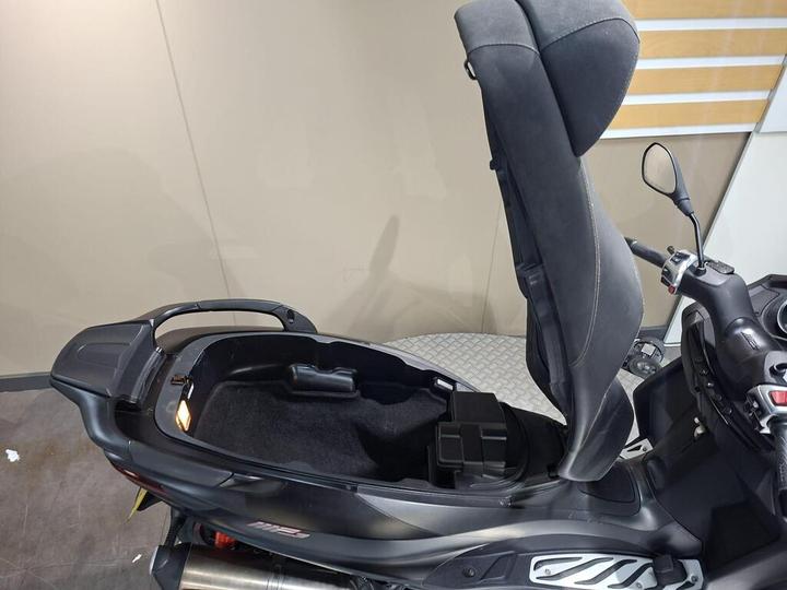 A close-up view of the interior of a scooter with a raised seat, revealing space for storage underneath, featuring a dark fabric lining and a small compartment.