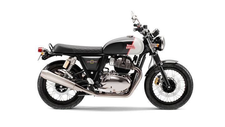 A Royal Enfield Interceptor motorcycle in a studio setting, featuring a grey fuel tank with the brand name in white, black seat, silver exhaust, and black frame with spoke wheels.