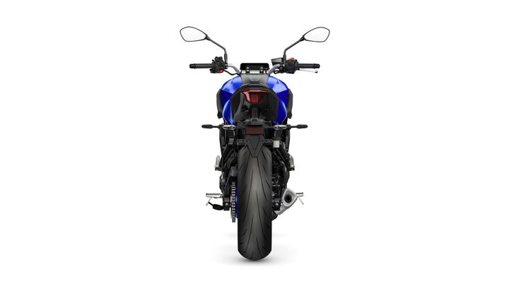 A rear view of a blue motorcycle with a prominent rear tire and distinctive tail light, showcasing the handlebars and mirrors.