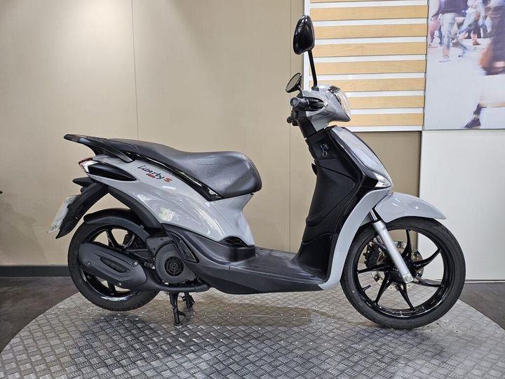 Piaggio Liberty S 125 (2021) A gray scooter, model Piaggio Liberty S, displayed on a textured surface with a neutral background.