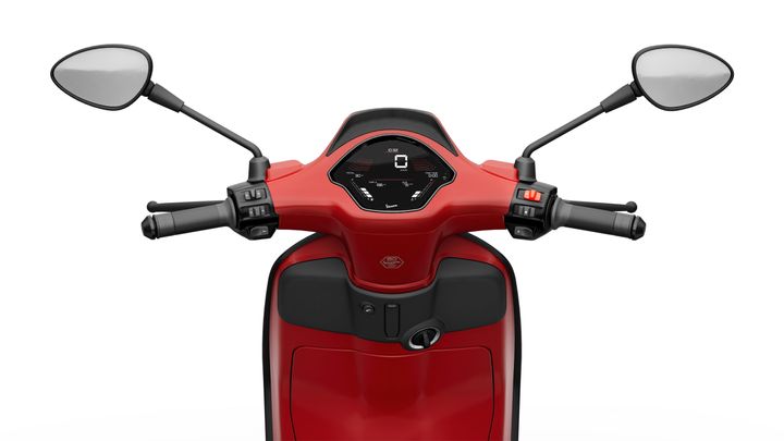 Close-up view of the handlebars and dashboard of a red scooter, featuring a digital speedometer and mirrors on either side.