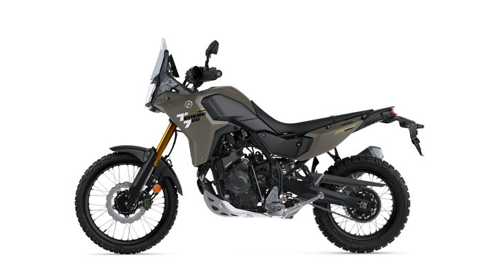 A side view of a Yamaha Tenere 700 adventure motorcycle in a muted green color, featuring knobby tires, a tall windscreen, and a sturdy frame designed for off-road riding.