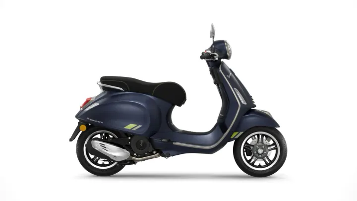 Alt text: A dark blue modern Vespa scooter stands in profile against a white background, featuring a sleek design with a black seat and accents of grey and lime green.