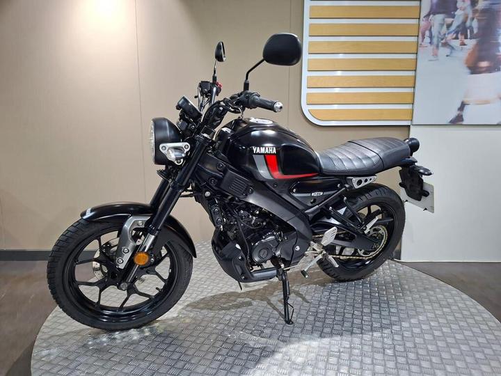 A black Yamaha motorcycle is displayed on a textured platform against a neutral background. The bike features a sleek design with a visible seat, handlebars, and the Yamaha logo prominently featured.