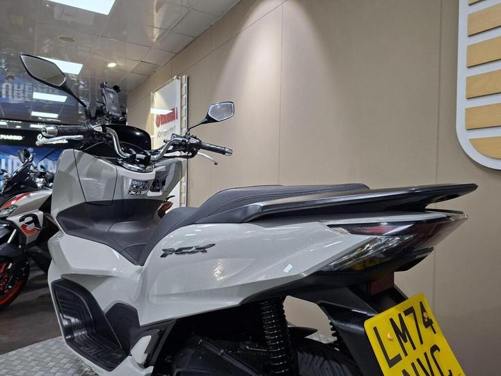 A modern gray scooter with a sleek design, showcasing its rear end and dashboard, displayed in a motorcycle showroom environment.