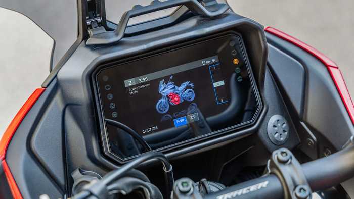 A close-up of a motorcycle's dashboard display showing power delivery settings, current speed at 0 km/h, and a 3D model of the bike with highlighted engine components.
