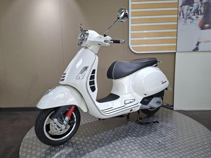A white Vespa scooter displayed on a circular platform with a modern interior backdrop.