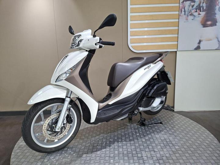 A modern white and brown scooter displayed on a circular metallic platform against a neutral background.