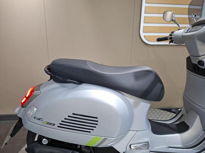 A silver scooter with a black seat, featuring a sleek design and a visible rear light, displayed against a neutral background.